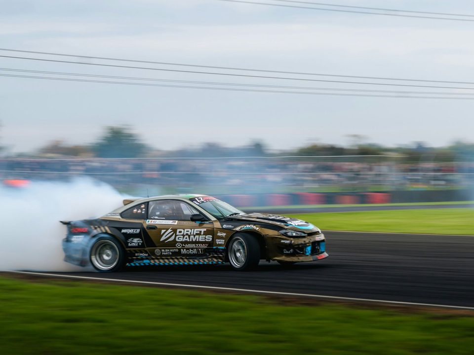 A drift car sideways in a wall of tyre smoke in front of a packed crowd.