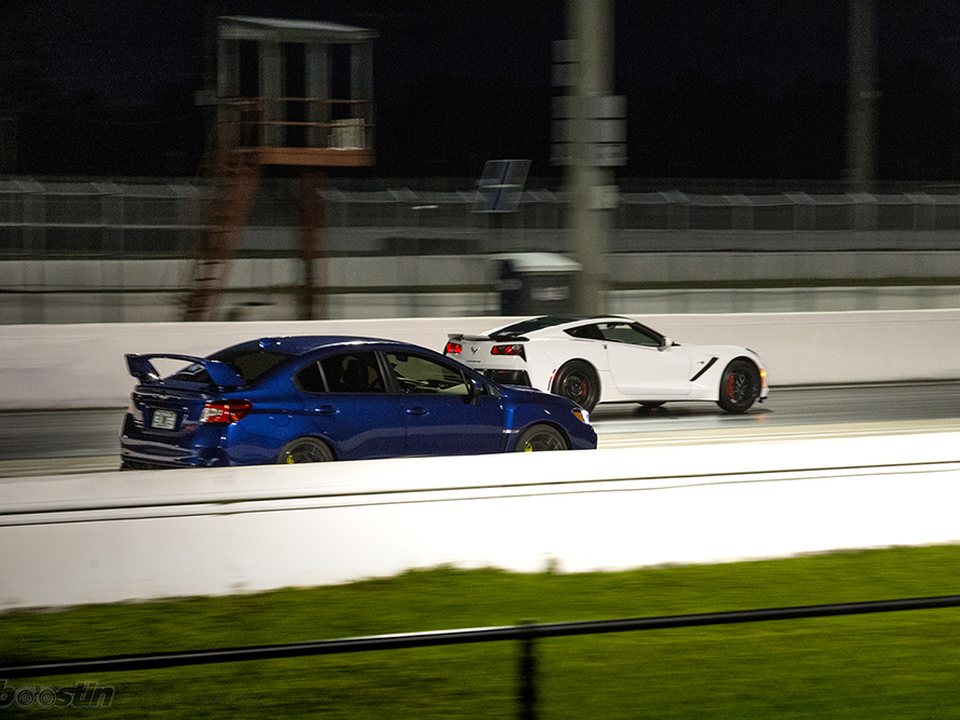 A WRX and a Corvette side by side on a roll racing run under lights.